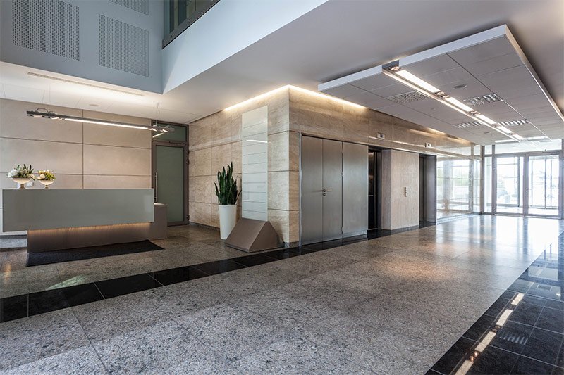 Corporate lobby viewing elevators and front desk with recessed track lighting along the walls, floors, and under desks